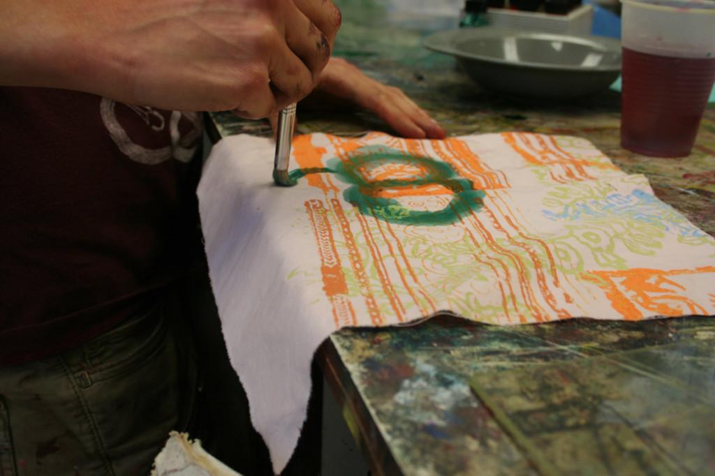 Visual senior in printmaking paints on a fabric print during class. 