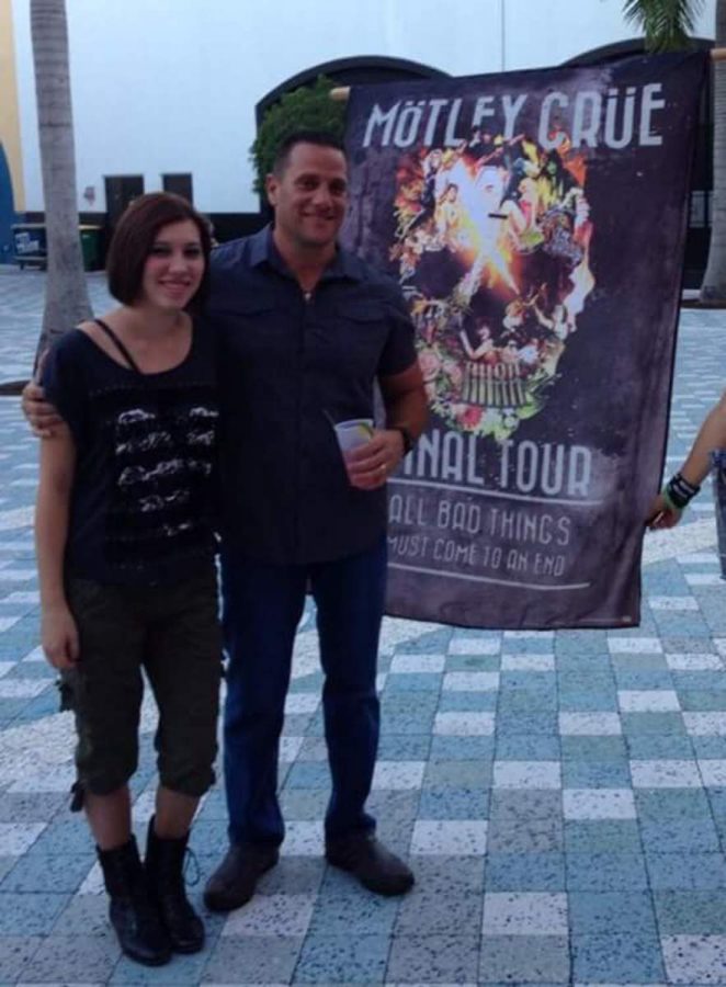 (L-R) Communications senior Briana Posner and her father pose with a promotional flag outside the venue for a Mötley Crüe concert.