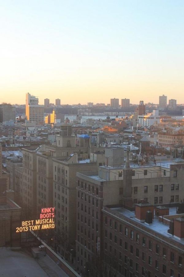 A New York City skyline taken from a rooftop at sunset. A nearby building displays an advertisement for the Tony award winning musical Kinky Boots . 