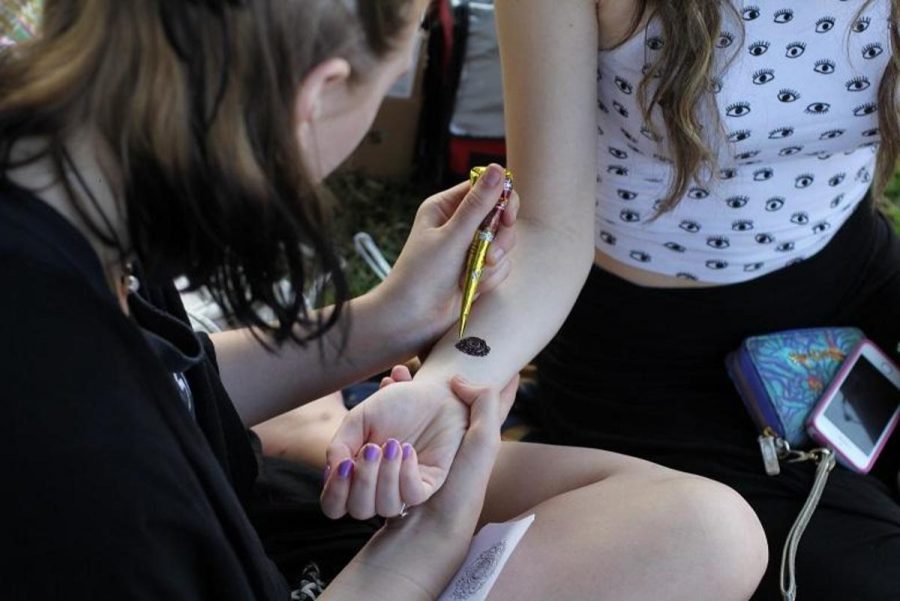 Visual senior Chloe Baur (L-R) gives theatre junior Melanie Margolese a henna tattoo during Fridays art sale. Students gathered on freshmen hill to purchase stickers, patches, clothing, and food made by their peers.
