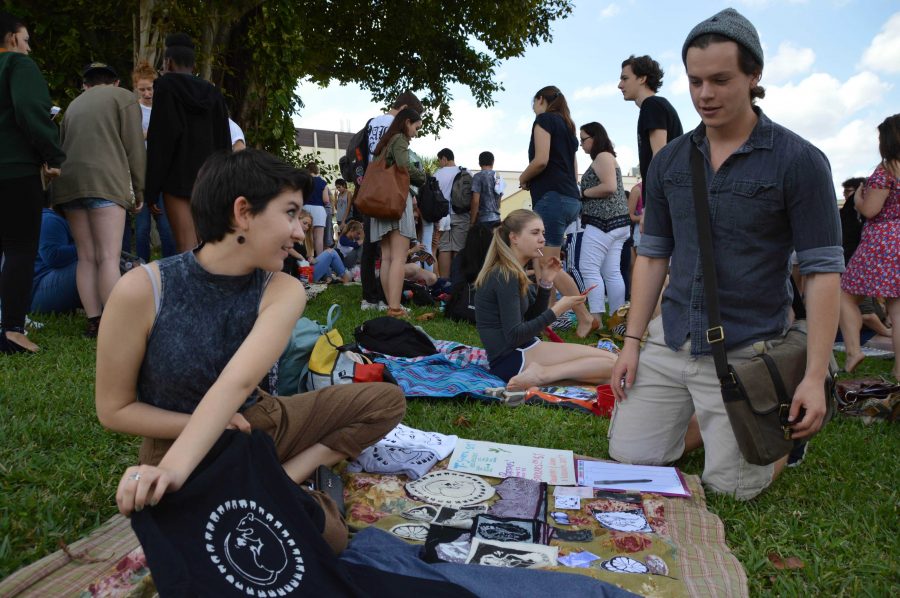 Visual senior Jailine Cano showcases her original artwork as a t-shirt design to digital media senior Casey McDonald at the last art sale of the 2015-2016 school year. The art sale, which takes place semi-annually on Freshman Hill, allows students to sell their artwork to other members of the Dreyfoos community. 