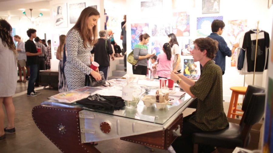 Theater junior Brandon Boyce sells raffle tickets and student designed clothing to attendees at the student art show held at Paul Fisher Gallery on May 13. The show was organized by digital media junior Michael Steinpichler and visual junior Brandon Fardella, along with Boyce and others. “I wasn’t expecting it to be so successful but I'm really proud of what me and all of my friends did,” Steinpichler said. 