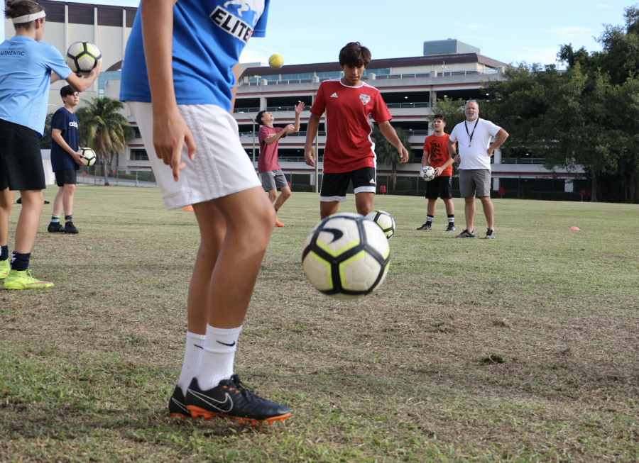 Theatre sophomore Xavier Zambrano pops the ball into the air with a swift kick as foreign language teacher and boys’ soccer coach Thomas Ruth watches the player’s technique.With both a new coach and new players, the boys’ soccer team has been preparing diligently for the season. Their first game is Monday, Nov. 12, at Palm Beach Lakes High School at 8 p.m.