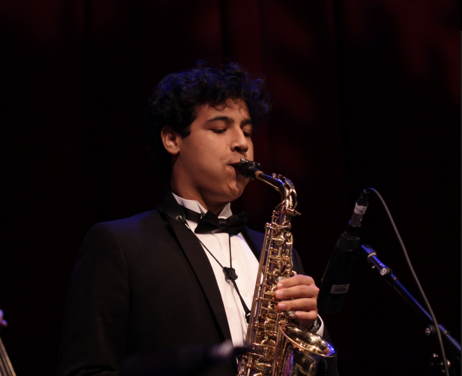 Band junior David Galli plays the saxophone alongside other performers at Prism. Behind the curtain, stage crew members moved instruments and equipment into place for the next performance. Piano junior Jacques Coury was among the stage crew members working behind the scenes. “There’s really not a dull moment [at Prism],” Coury said. “We’re always doing something, and there’s always something we can be doing to make [the performance] run smoother.” 
