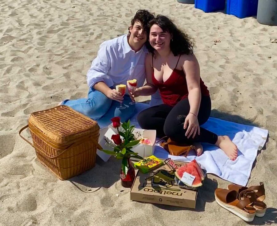 Kayla Esther Zakarin, right, and her boyfriend, left, sit on the beach holding wine glasses filled with cake.