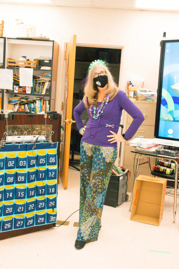 English teacher Martha Warwick poses in a Mardi Gras ensemble, pairing vibrant pants with a layer of purple, gold, and green beads. These colors are traditionally associated with the holiday and have been assigned to symbolize justice, power, and faith respectively. Photo by Allison Robbert.