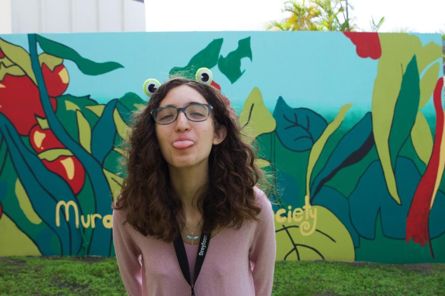 As president of Mural Painting Society, visual senior Jackie Cohen poses in front of the club’s first on-campus mural, which was created in collaboration with the Good Thyme Gardening Club. Cohen can often be spotted around campus sporting a headband or hat with frog eyes because she “just like(s) frogs.”