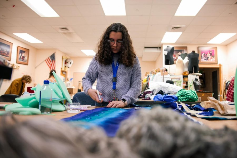 Surrounded by foam cutouts for the morph suits of the plant roots, theatre freshman Elizabeth Kronhaus cuts a piece of fabric as actors are fitted for their other costumes in the shop.