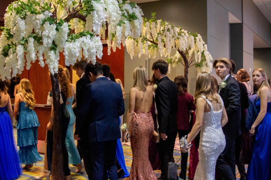 Students move from the lobby to the ballroom after mingling and eating, entering under a floral arch.