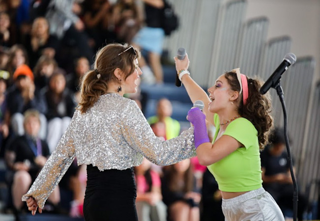Performing Lady Gaga’s “Poker Face,” dance sophomore Sophie Izenwasser and strings sophomore Isabella Cecere share microphones as the final part of the bridge echoes through the gymnasium. 
