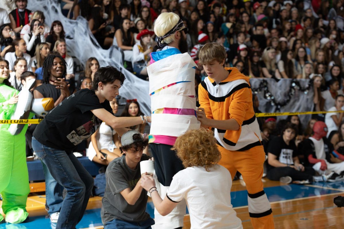 Theatre seniors Tyler Schmaling (left) and Lucas Lacy (right) wrap math teacher Timothee Freeman during the Mummy Wrap contest at the Fall Festival.