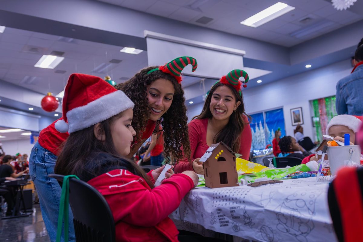 Theatre junior Kirra Bevilacqua and digital media junior Elysa Escobar help kids build model gingerbread houses, do arts and crafts, and other activities at the Jefferson Jubilee. Members from Arts Club signed up to buy and distribute gifts for kids in addition to helping during the annual event to hosted for underprivileged kids from all over palm beach county
