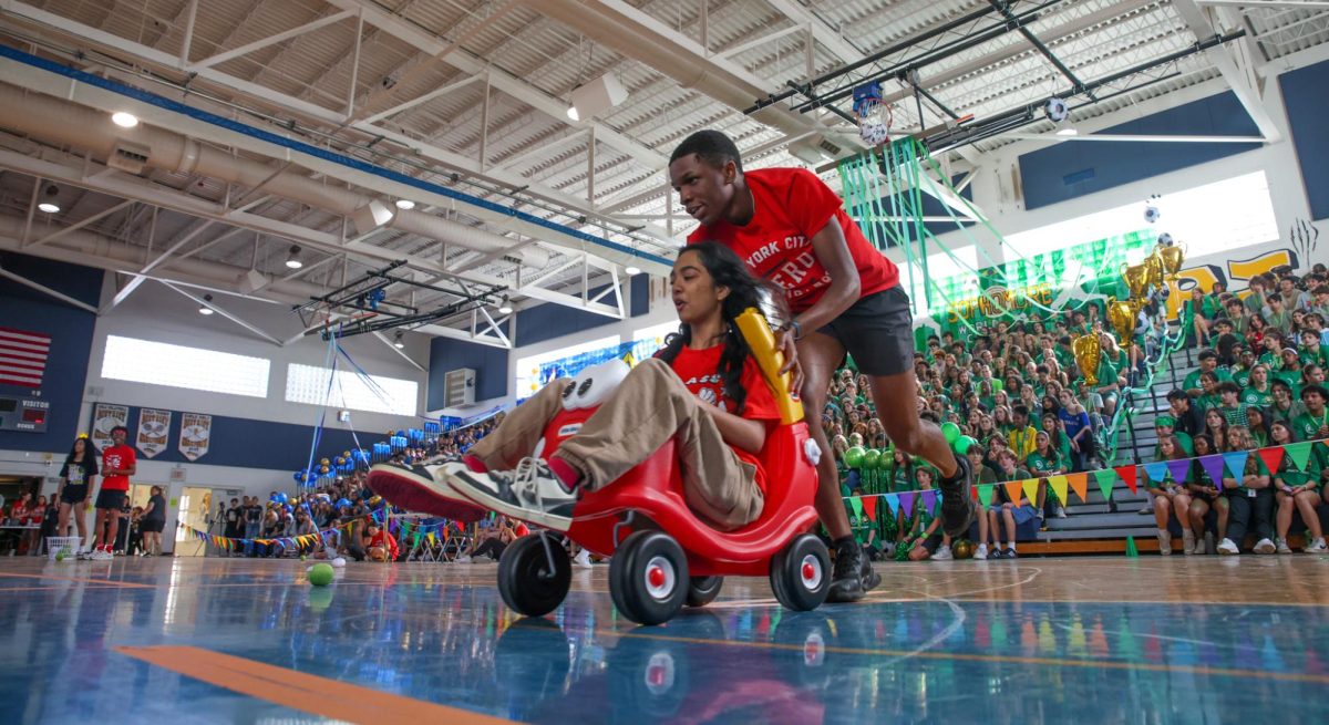 Band junior Roodley Blaise pushes junior class council co-president and communications junior Raiqa Rayhan during the Mario Kart game. Participants had to race around a course taped out on the gym floor. 