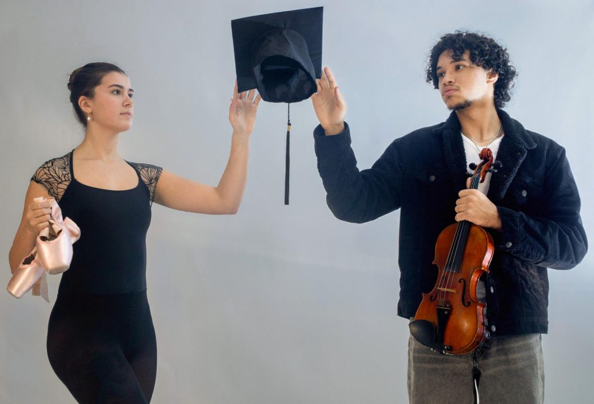 Reaching for a graduation cap, dance senior Lilly Foster and strings senior Vincenzo Serra hold their pointe shoes and violin, respectively. According to Foster, getting to graduation has been “a challenge” because of her extracurricular commitments. “After school, I go to the dance studio, and I'm also (part of my studio’s) dance company,” Foster said. “It's both of those things together, attending (dance) classes at school every day and going to the dance studio (right away) from (4 p.m.) to (9 p.m.) most nights, (that) is really difficult.” 
