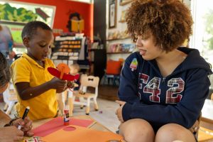 Interacting with a pre-school learner, Justice Builder intern and digital senior Aaliyah Keys helps lead the day’s craft activity centered around the letter “I.” As part of her paid internship at Rohi’s Readery, which focuses on community outreach and social justice education, Keys prepared pre-made craft pieces for the children to easily assemble an insect.