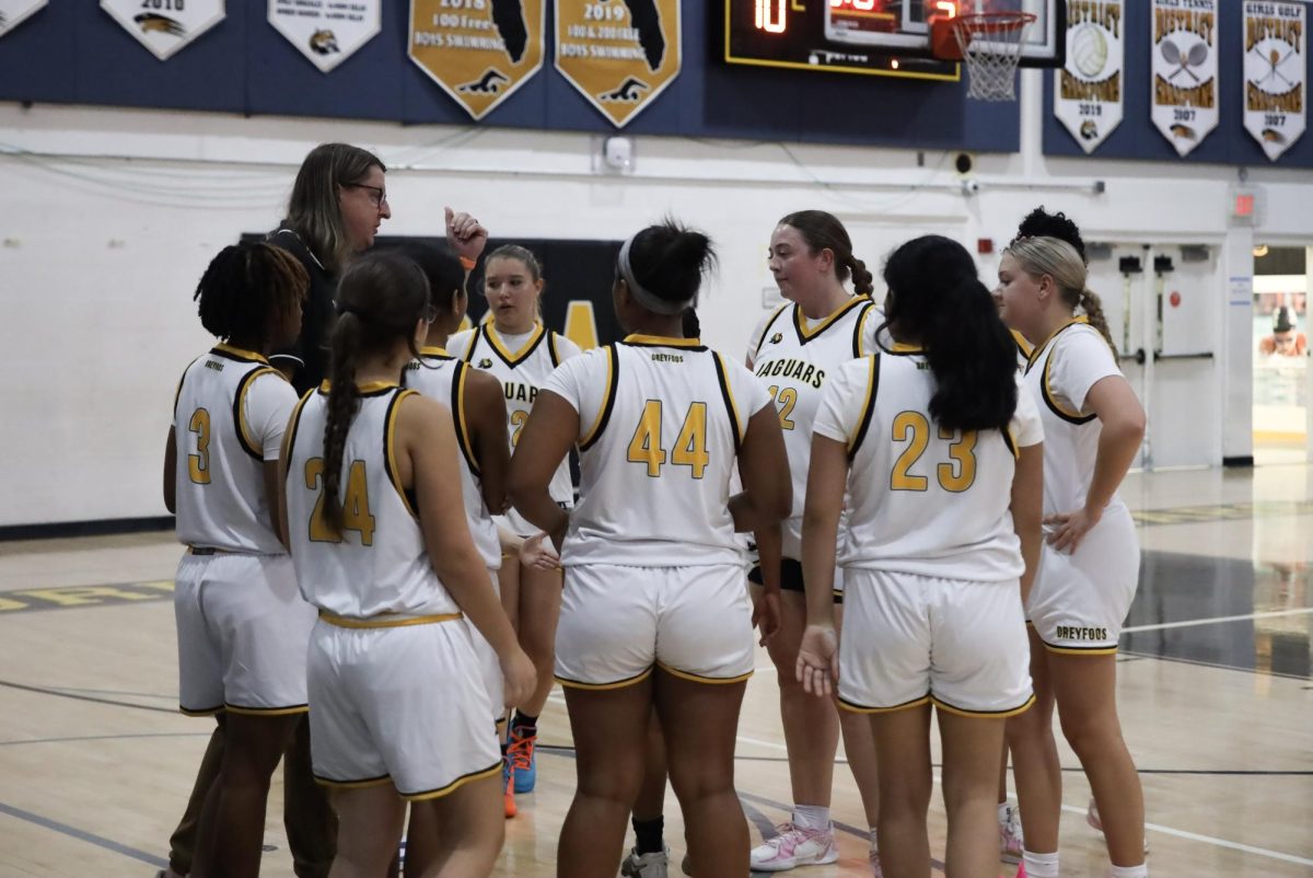 Convening with their coach, Mr. Millstein to discuss game strategies, the girl's basketball team plans for the match during a time out.