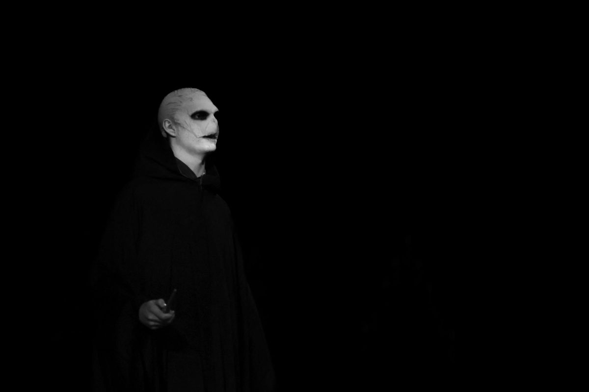 Looking out towards the audience, theatre senior Ross Patrick (Voldemort) stands in darkness. This scene occurs in Act 2 after a body switch conducted with the assistance of smoke machines and lighting.