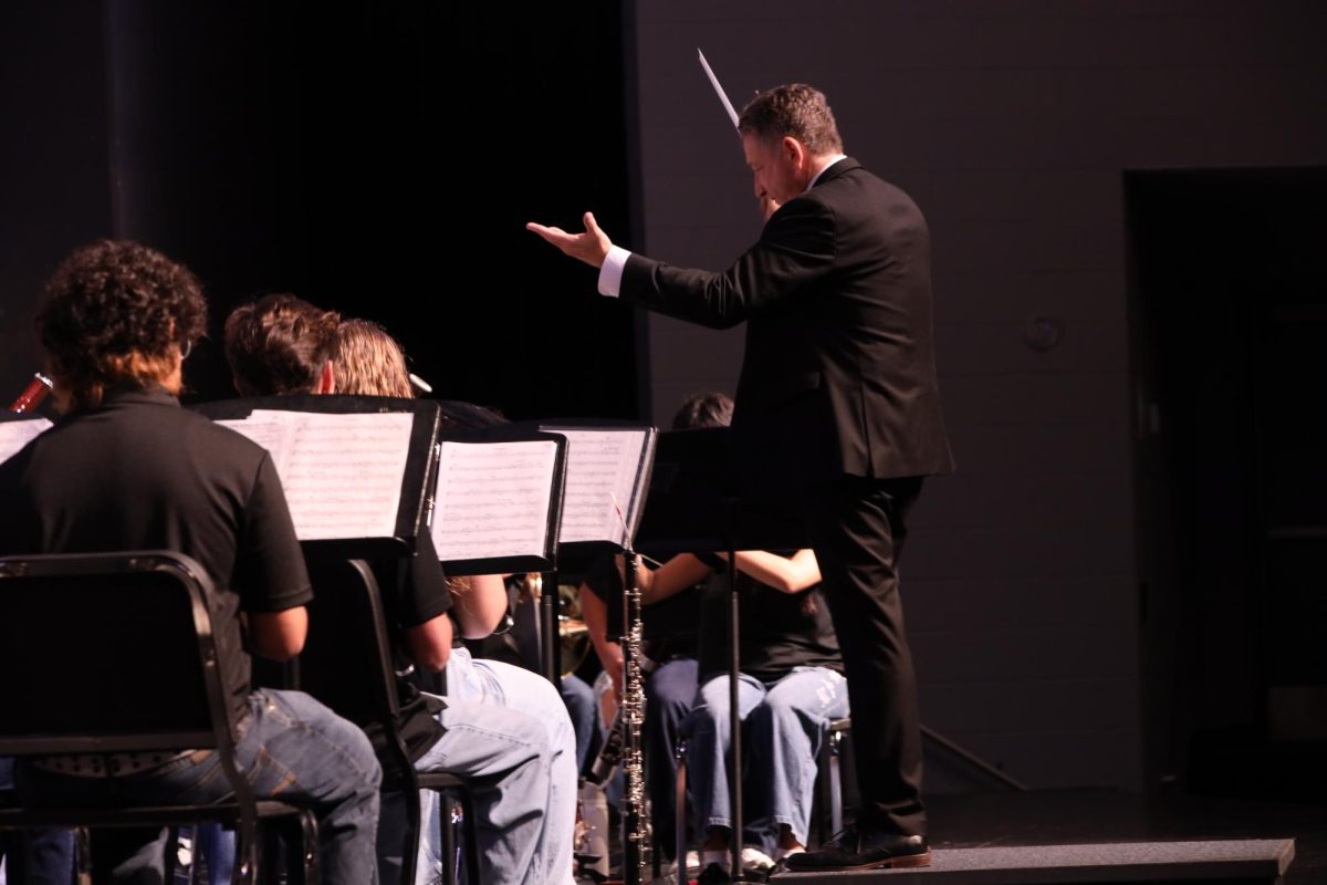 Directing the band, band director Evan Rogovin raises his hand and baton. 