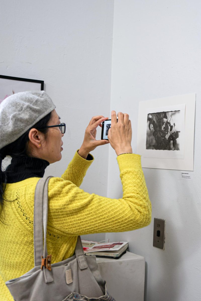 Taking a photo of a student’s artwork, an exhibition attendee observes the artwork.