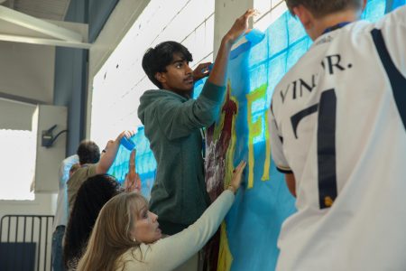Taping his class (freshman) banner to the gym wall, communications freshman Arjun Kuturu assists in hanging up the “Fantastic Freshmen” sign. The banner took inspiration from the “Fantastic Four” series.