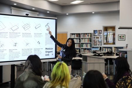 Directing students to the screen, Asian Cultural Society guest Lynn Min presents the origami folding process. The craft originated in China and was used in religious ceremonies for wrapping gifts.
