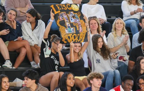 Watching the game, visual juniors Isabella Rigaud and Coco Dobbins hold up a handmade poster to support vocal senior and defense specialist Jack Meller.